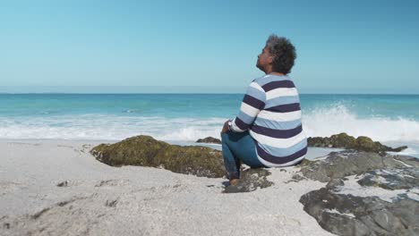 Ältere-Frau-Sitzt-Auf-Einem-Felsen-Am-Strand