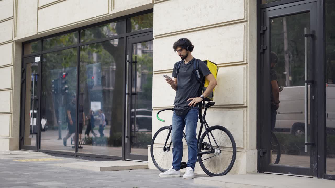 Courier with backpack waiting on a address point, leans on a bike