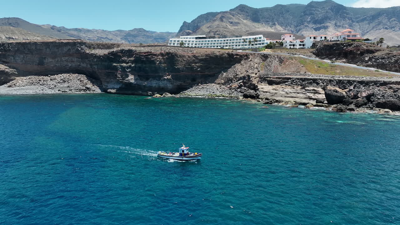 monitoreo aéreo de un barco de pesca que cruza las aguas turquesas del puerto de agaete en un día soleado