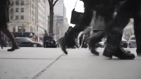 people hurry along the sidewalk in a bustling urban environment, their shoes striking the pavement amid the sounds of the city. the scene captures the energy of daily life in a metropolitan area.