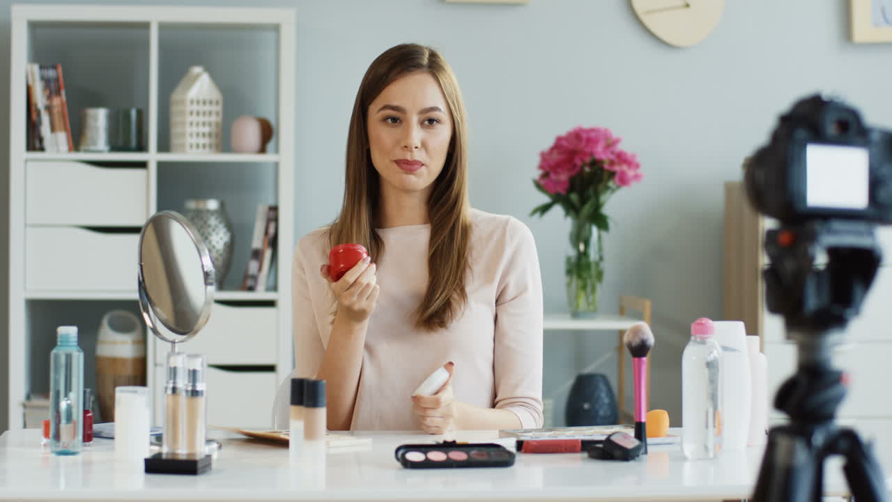 bastante joven bloguera de belleza abriendo y oliendo una crema facial mientras graba un video en casa