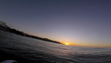 Joven-Surfista-Con-Casco-Blanco-Se-Sienta-En-Línea-Durante-La-Sesión-De-Surf-De-La-Mañana,-Espera-Su-Ola-Y-Disfruta-Del-Cálido-Amanecer-Tropical