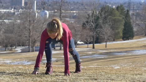 blonde woman in boots and sportswear stretches her legs in the park on the yellow grass in the winter