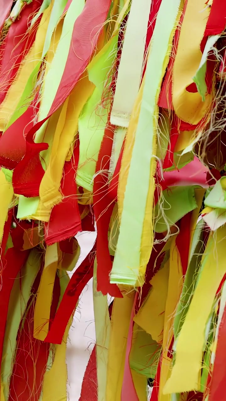 Primer plano de vibrantes ofrendas de tela rojas, amarillas y verdes mecidas por la brisa