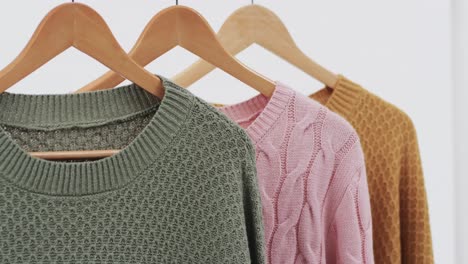 video of three multi coloured sweaters on hangers and copy space on white background