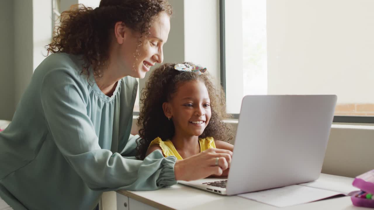 Video of happy caucasian female teacher explaining lesson on laptop to african american girl