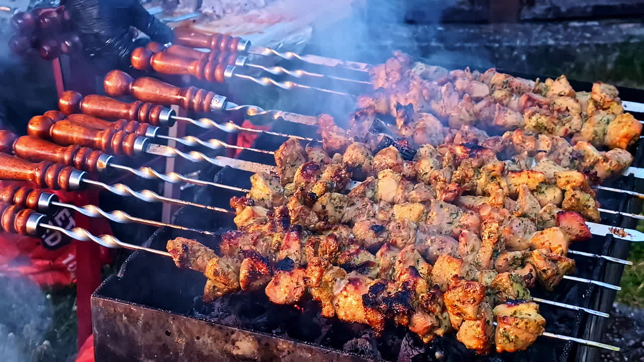 Juicy meat sticks are turned on a large grill, sizzling under open air heat