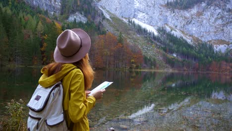 girl explorer with the backpack  traveling and looking at the touristic map  at the beautiful mountain lake