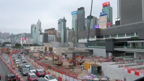 cranes, metal girders, and engineering equipment stand on a construction site as part of a redevelopment commercial project while the hong kong financial district skyline is in the background