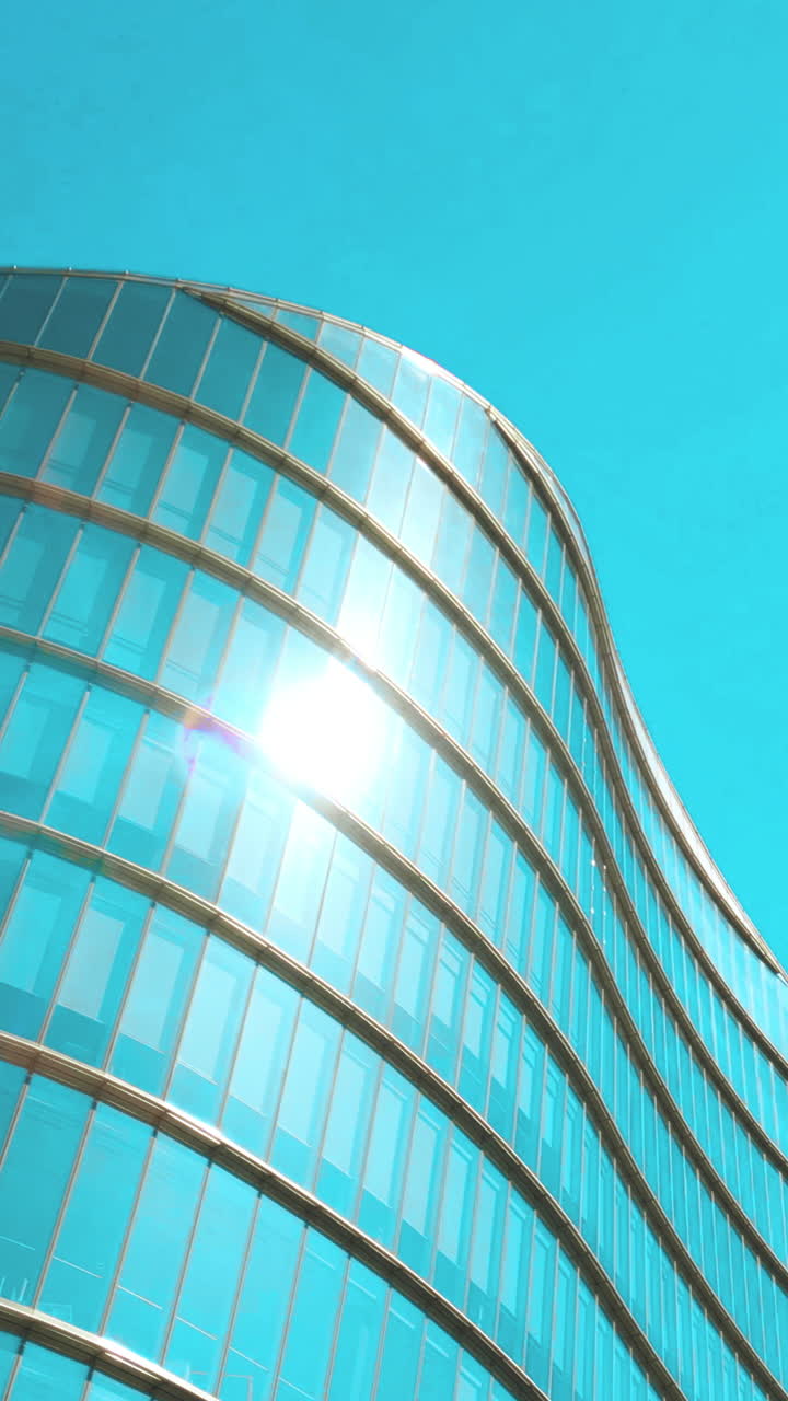 Perspectiva Ascendente de Edifício Moderno de Vidro Refletindo o Sol e o Céu Azul