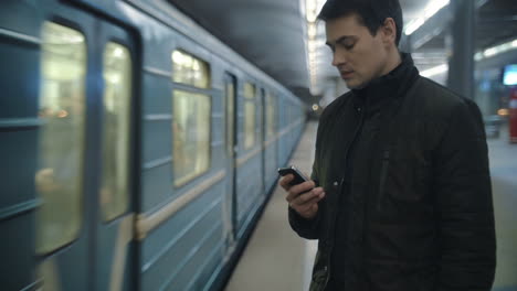 hombre escribiendo sms de pie en la plataforma del metro