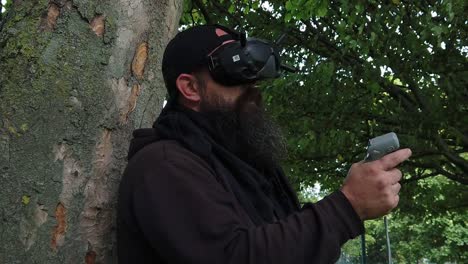 bearded male wearing virtual fpv goggles controlling drone in park with motion joystick