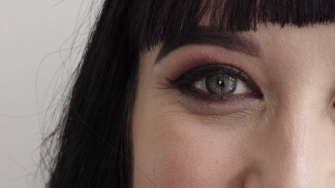 de cerca ojo de mujer con maquillaje mirando feliz a la cámara parpadeando belleza cosméticos mitad de la cara