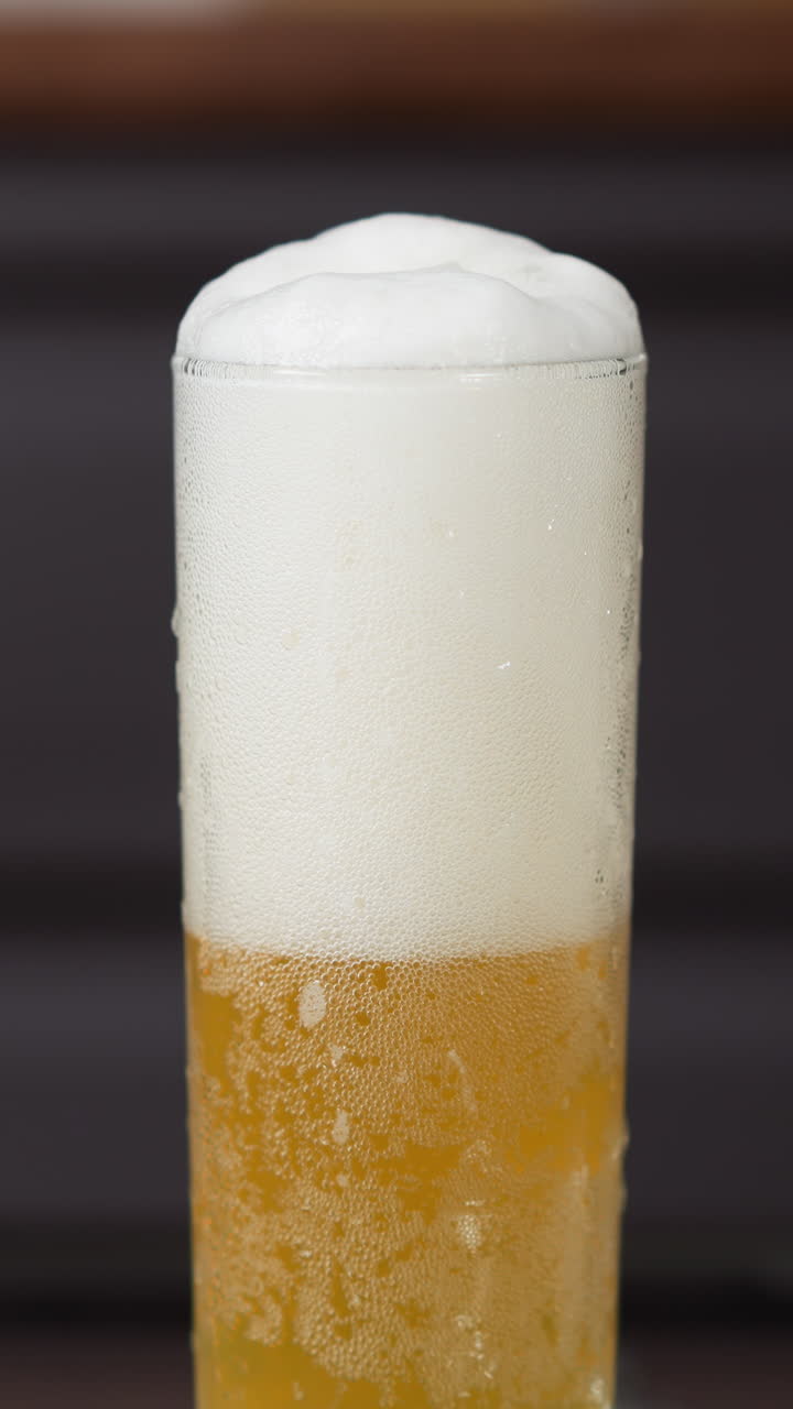 cerveza dorada espumosa que se vierte en un vaso alto con burbujas ascendentes y cabeza de espuma