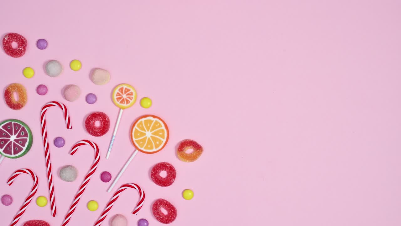 Fundo rosa pastel com doces, balas e pirulitos em movimento. Flat lay em stop motion.