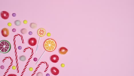 pastel pink background with moving sweets candies and lollipops. stop motion flat lay