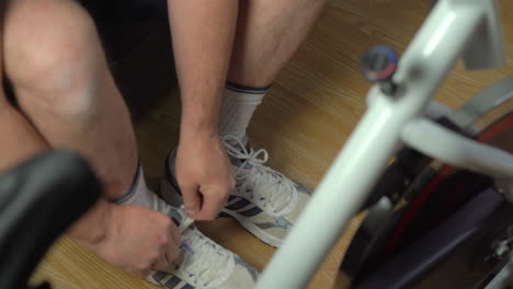 Sneakers-being-laced-up-by-man-with-exercise-bicycle-in-foreground