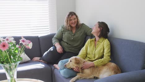 Caucasian-lesbian-couple-smiling-and-sitting-on-couch-with-dog