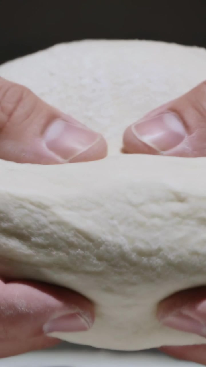 Video verticale: Mani di un cuoco che accarezzano e premono una palla di impasto rotonda e chiara sul bancone, modellandola per la cottura