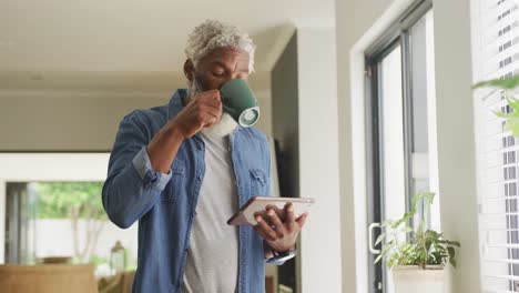 Video-Eines-Afroamerikanischen-älteren-Mannes,-Der-Kaffee-Trinkt-Und-Ein-Tablet-Benutzt