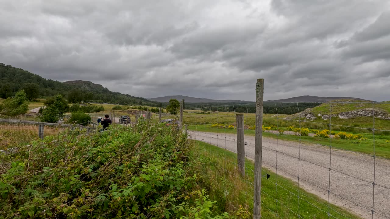 Car halts on winding rural road, overcast sky, lush green hills, static wide landscape shot