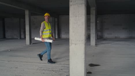 imagen amplia de un ingeniero caucásico caminando por el sitio de construcción y sosteniendo planes de proyecto.