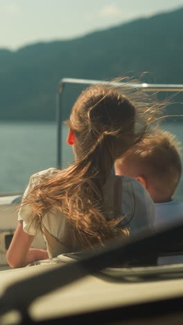 cheerful little children enjoy view from cabin exit riding motorboat in scenic sea. focused brother and sister sail modern yacht in ocean on summer holiday