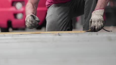 steelworker measuring metal using tape measure in a workshop - ground-level shot