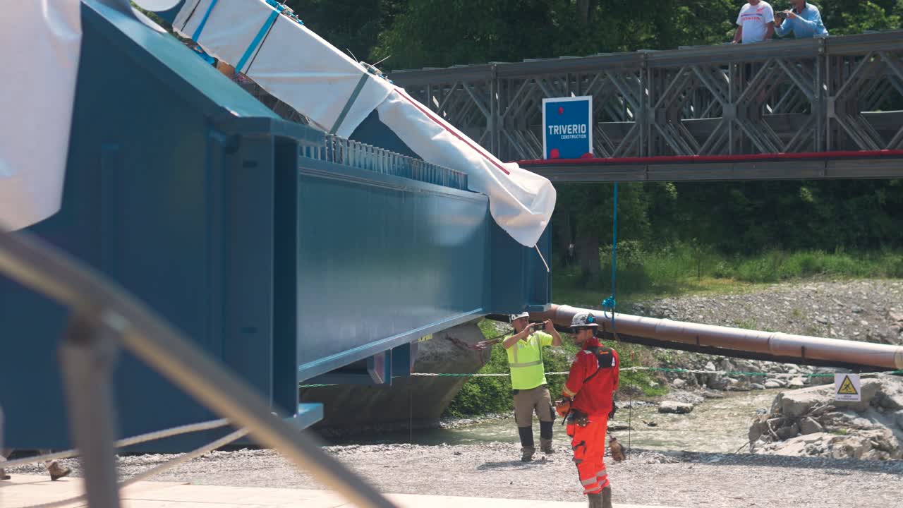 Rigging crew guides large bridge structure into place at construction site in Tende, France