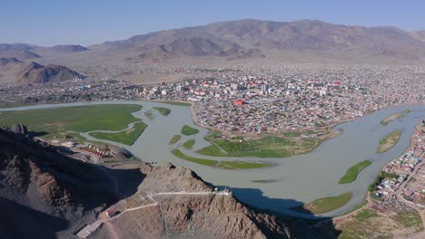 aerial shot of ulgii village and river with green areas and mountains landscape, mongolia