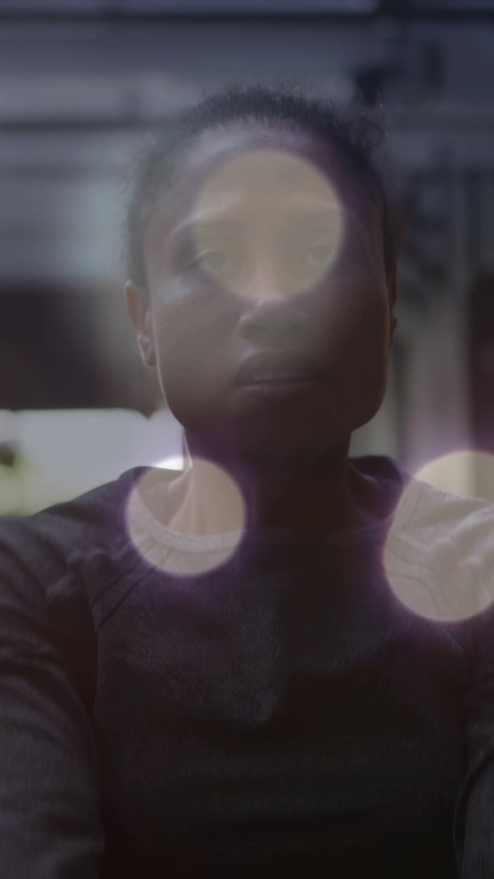 Vertical video: Woman lifting hands toward camera to peer through bokeh, framing face in film set