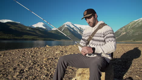 wide - medium shot of a male fisherman prepping a fly fishing rod and reel