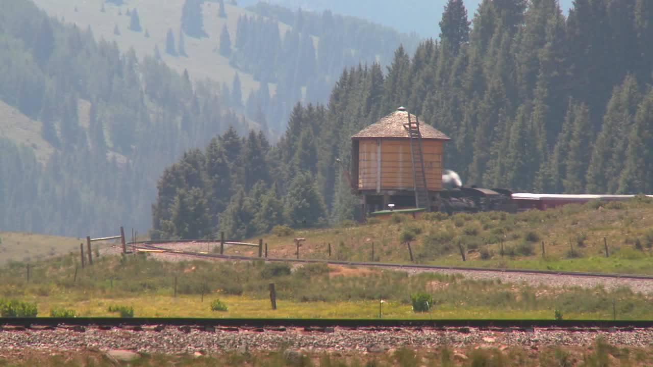 un tren de vapor pasa una torre de agua a lo largo de las vías