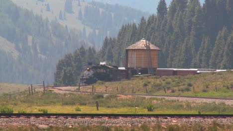 a steam train passes a water tower along the tracks