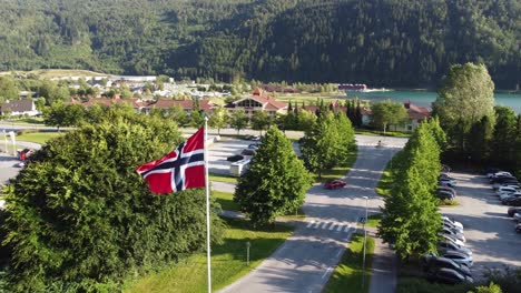 norway flag beautifully blowing in the wind with loen towncentre and fjord in background - slowly moving aerial in beautiful landscape environment - loen nordfjord norway