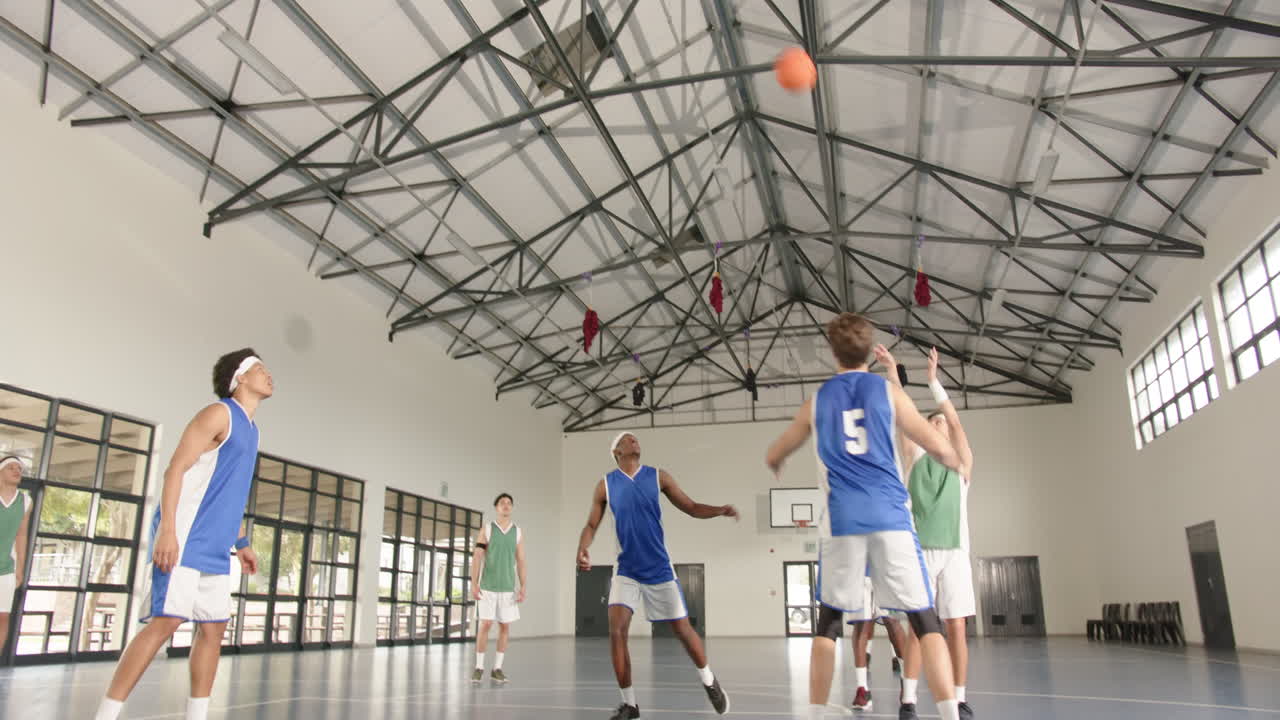 In gym, basketball players watching ball during intense game, focusing on action