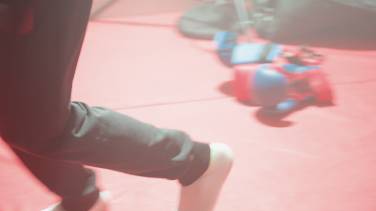 Close-up of legs in black pants and white socks moving on red gym mat, capturing dynamic motion, athletic energy, fitness training atmosphere, showing detail of exercise activity lower body movement