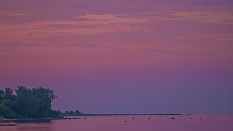 timelapse shot of purple and pink sky over the sea just after sunset along the shoreline during evening time