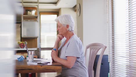 Senior-caucasian-woman-holding-medication-bottle-while-having-video-chat-on-laptop-at-home