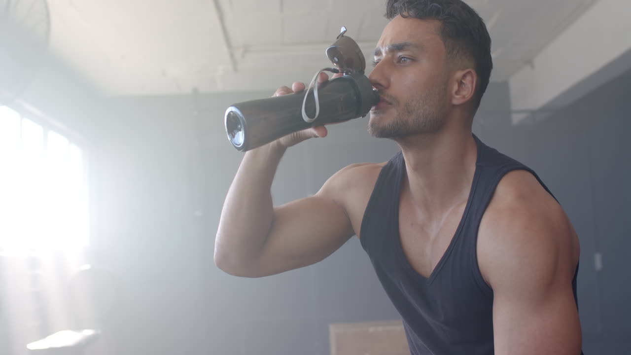 Strong and fit biracial man in gym drinking from black water bottle
