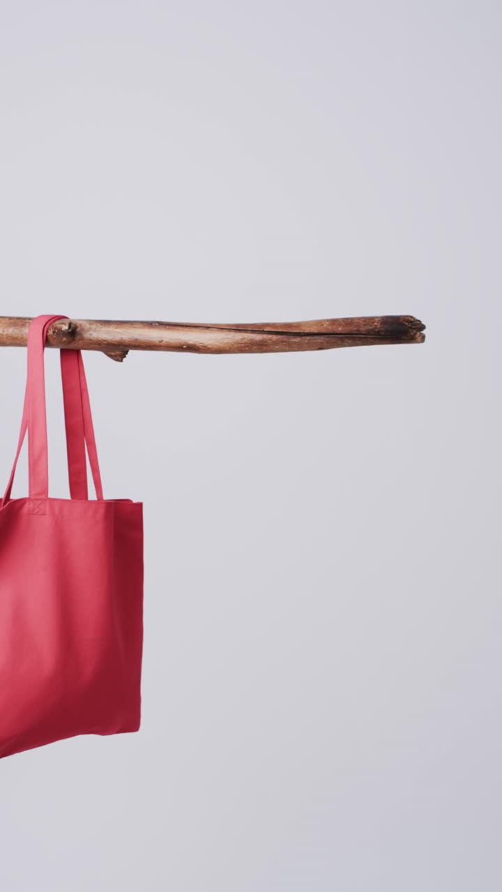 Vertical video of red canvas bag hanging from branch with copy space on white background