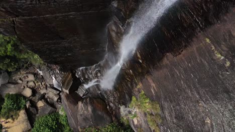 una pequeña corriente de agua cae desde una gran altura sobre las escarpadas paredes montañosas de la cascada del salto de los amantes en sri-lanka entre la naturaleza verde