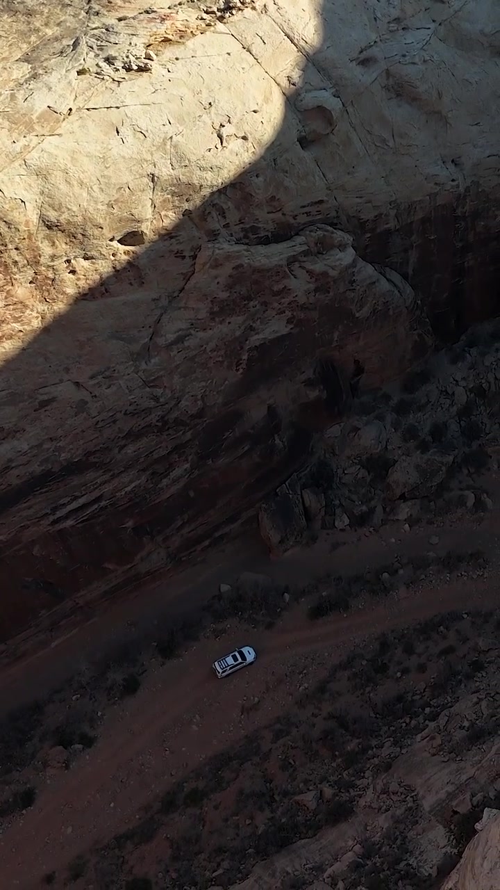 Ripresa verticale con drone di un'auto SUV bianca che si muove su una strada in un canyon profondo, Utah, USA.
