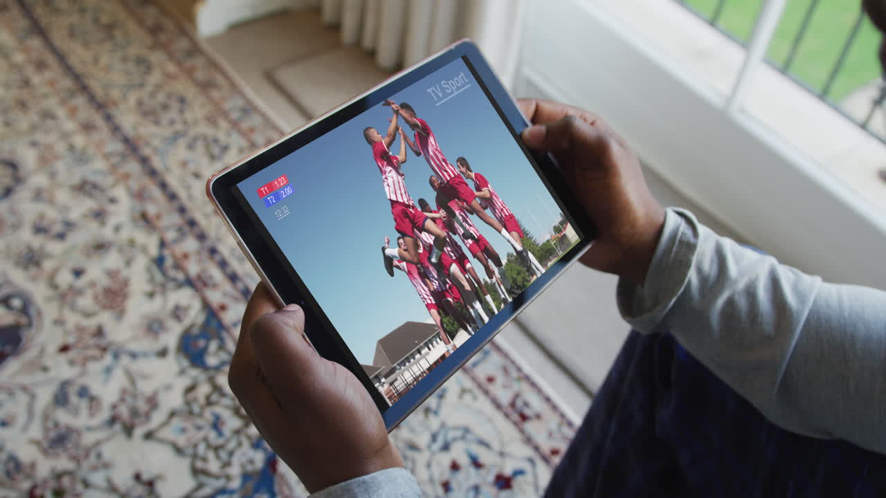 Composite of man sitting at home, watching sports event on tablet