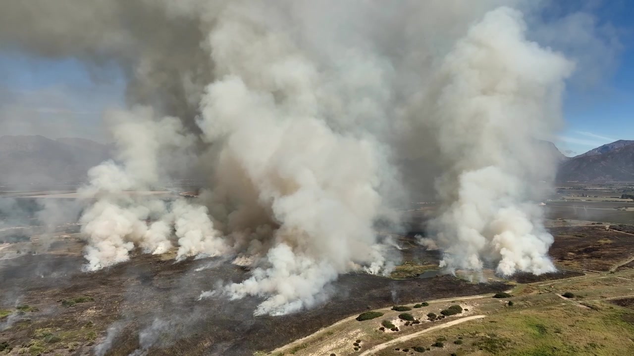 Riprese aeree circolari di un incendio di erba su un altopiano montuoso che riempie il cielo di fumo denso