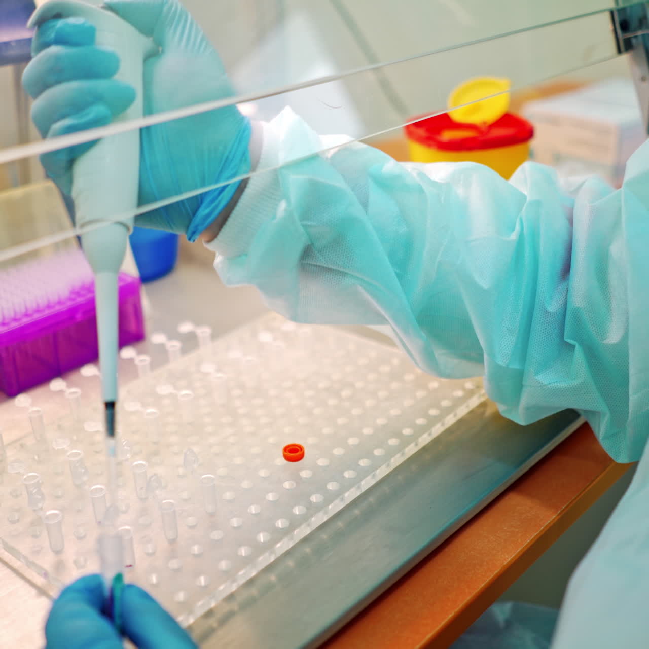 Medical assistant works with test tubes. Researcher in protective uniform dripping liquid into vials with special instrument. Close-up.