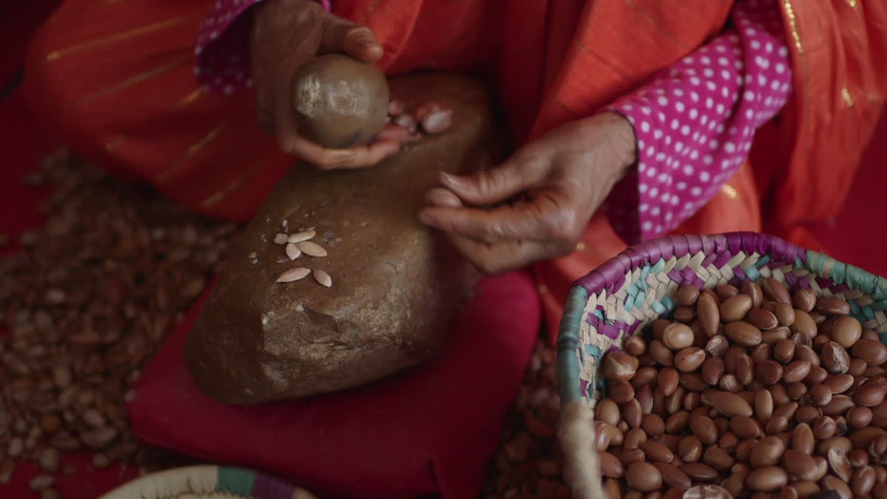 바위로 아르간 씨앗을 부수는 화려한 드레스를 입은 모로코 여성