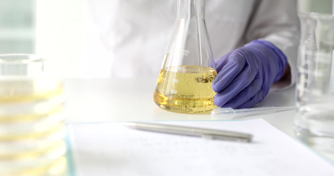 Scientist pours liquid into flask on bright laboratory table