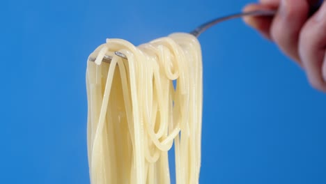 mano masculina sosteniendo un tenedor con espagueti de pasta hervida.