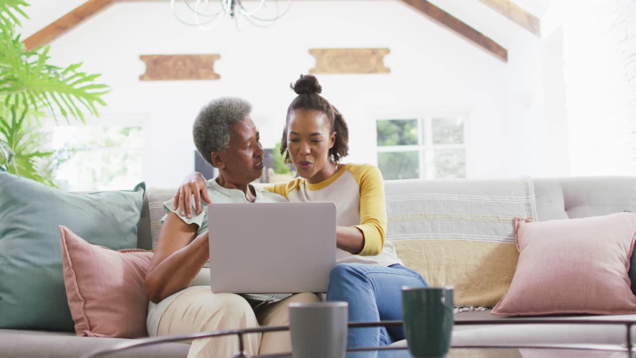 African american mother and daughter smiling while using laptop together at home